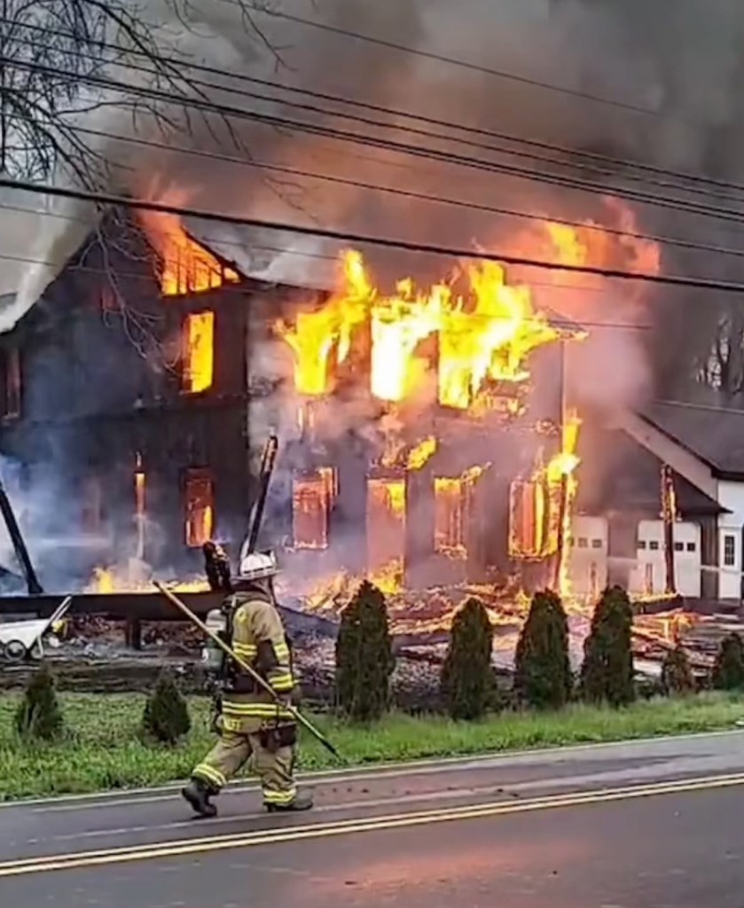 A firefighter stands before a house engulfed in flames after an explosion.