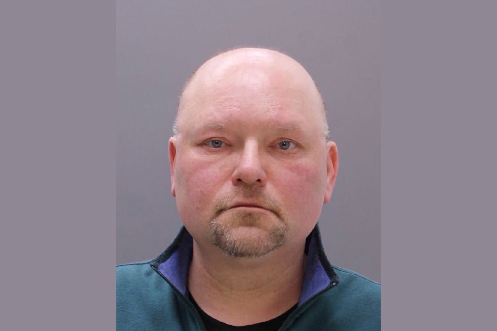 Mugshot of a bald man with a short goatee, wearing a green jacket over a black shirt.