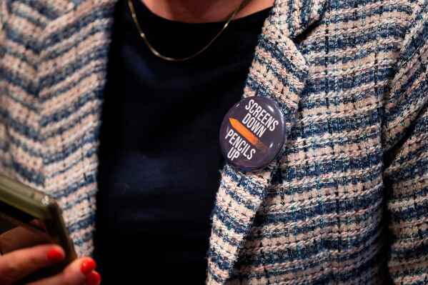 An attendee wears a, "Screens down, pencils up," button during a school board meeting at the Lower Merion School District Administration Building on Monday, May 11, 2026, in Ardmore, Pa. (AP Photo/Joe Lamberti)