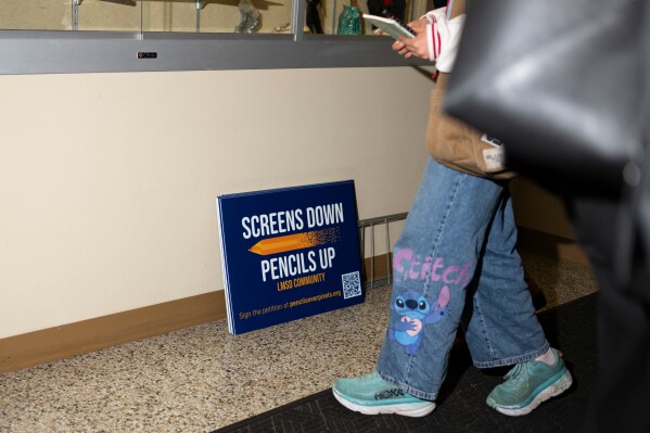 Signs reading, "Screens down, pencils up," are seen a school board meeting at the Lower Merion School District Administration Building on Monday, May 11, 2026, in Ardmore, Pa. (AP Photo/Joe Lamberti)
