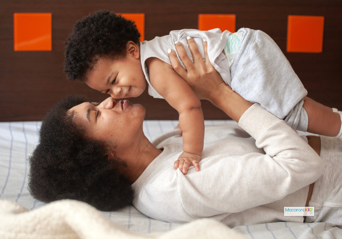 Mom lying on a bed laughing and playing with her toddler,  a joyful everyday parenting moment