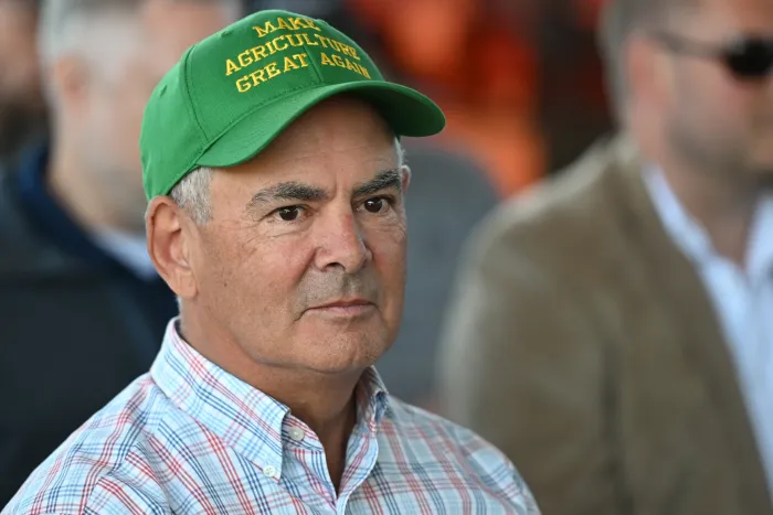 A close up of an older man in a green baseball had that reads, "Make Agriculture Great Again." 