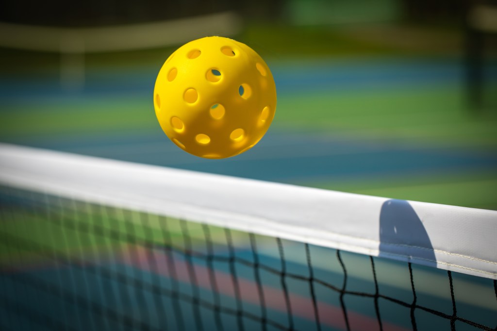 Yellow pickleball crossing a pickleball net with a shadow on the top tape.