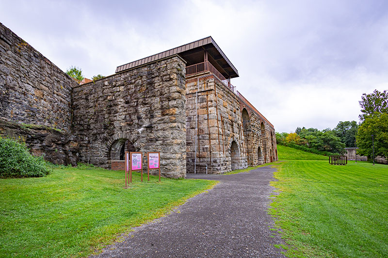 The Scranton Iron Furnaces in Scranton, PA, are a historic industrial site with large stone structures, arched openings, and informational signs, surrounded by green grass and a pathway.