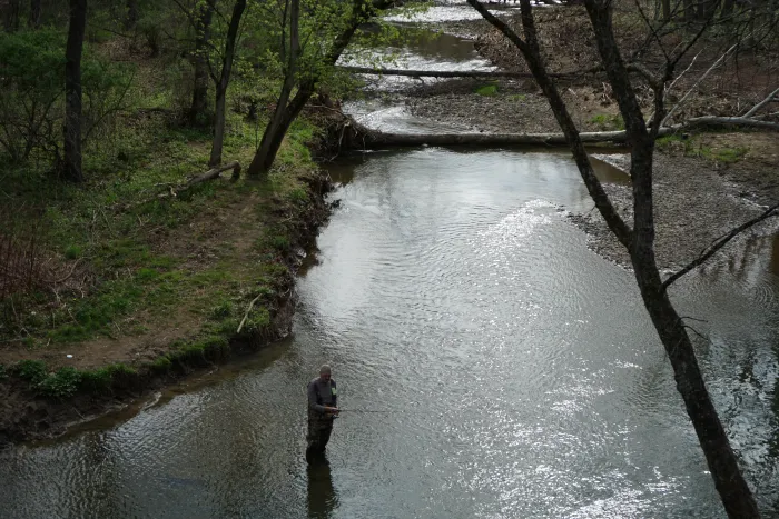 Seen from above, a man stands in a stream fishing.