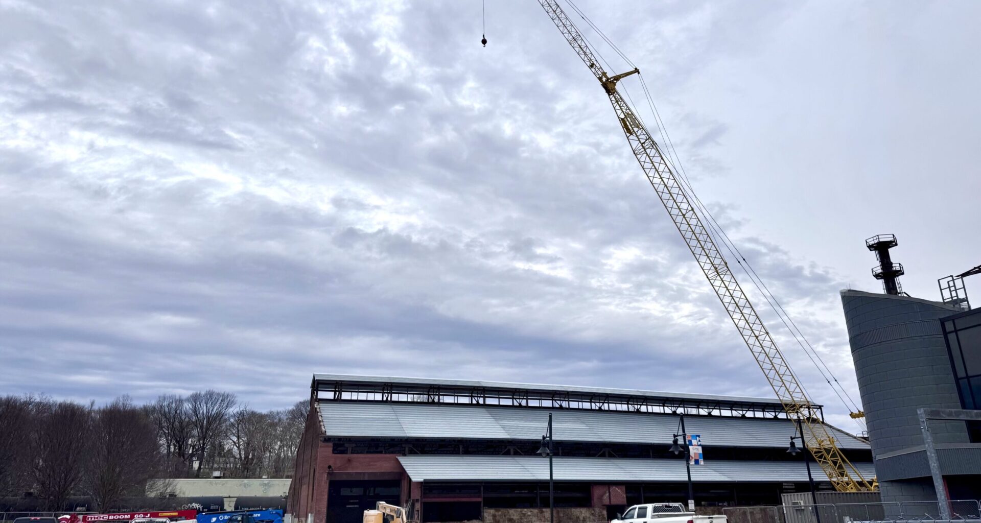 a construction crane rises above the brick turn & grind shop building at steelstacks in bethlehem, with a partially installed metal roof, work vehicles and fencing in the foreground under an overcast sky