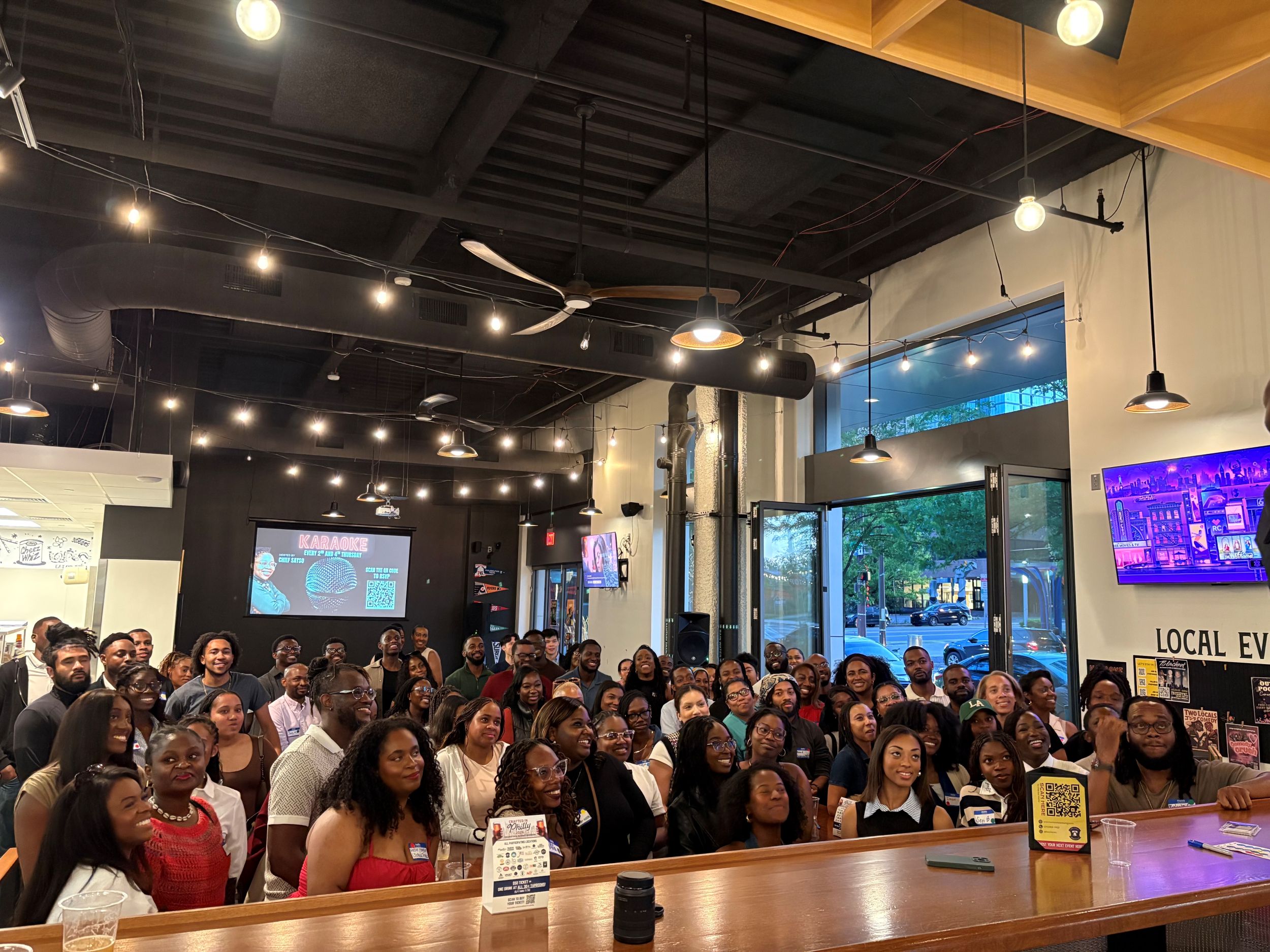A large group of people pose and smile for a photo inside a modern, well-lit venue with high ceilings and large windows.