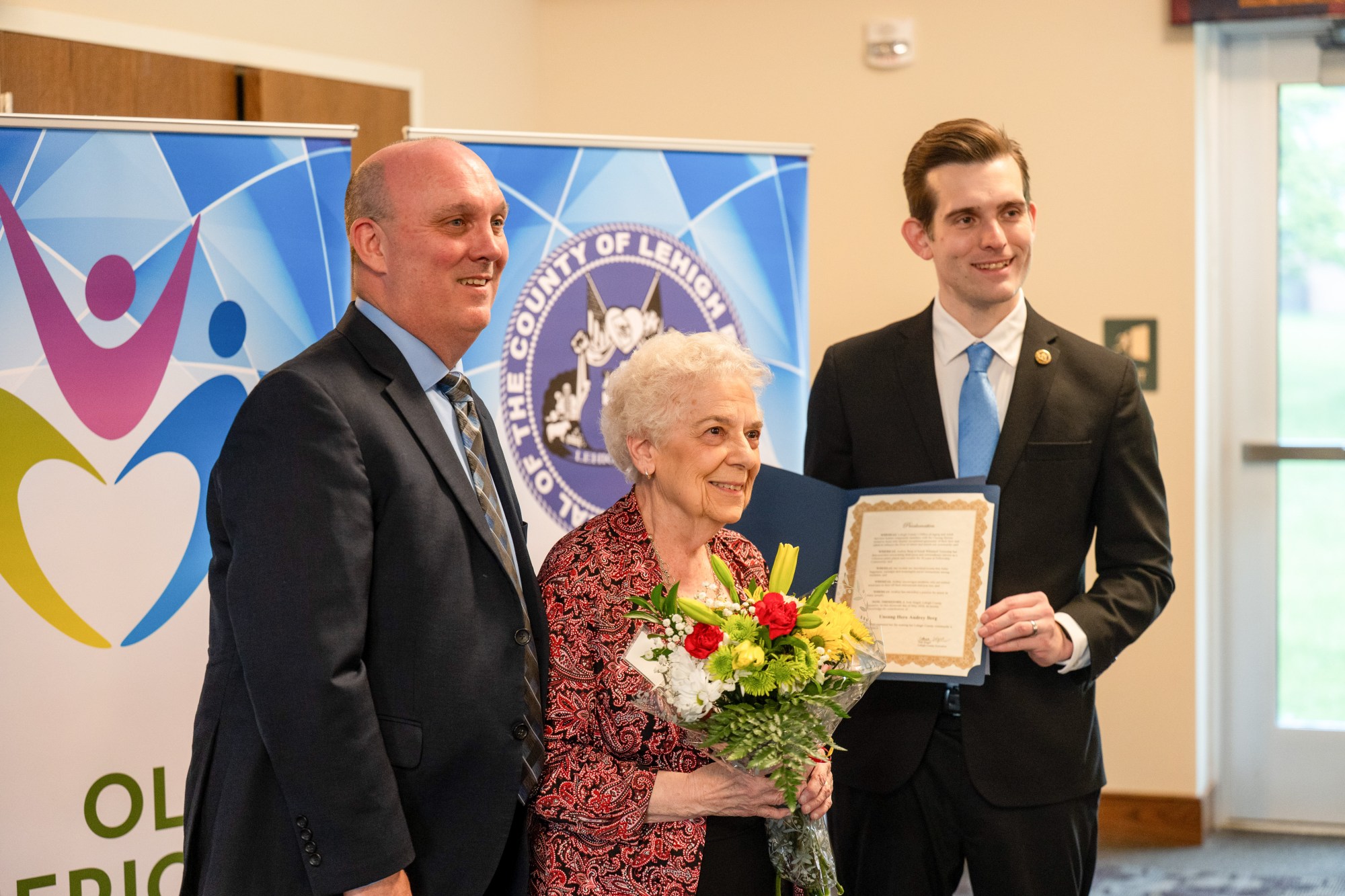 Lehigh County Aging & Adult Services Executive Director JR Reed and Lehigh County Executive Josh Siegel present an award to Audrey Berg of South Whitehall Township during the 26th annual Unsung Heroes tribute Wednesday, May 13, 2026, at Fellowship Community's Zentz Center in Whitehall Township. The annual tribute recognizes older adults who have enhanced their communities through active engagement, volunteerism and service to others. (Jonathan Broady/Special to The Morning Call)