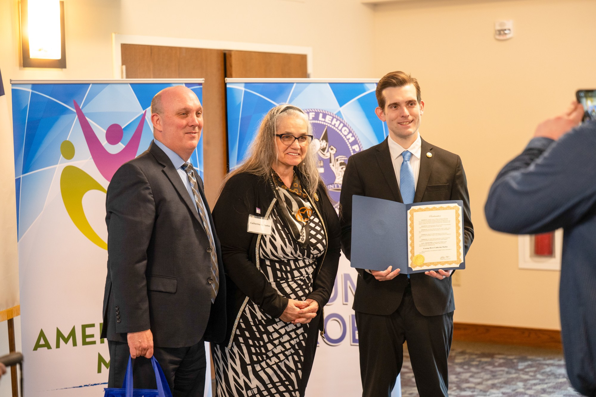 Lehigh County Aging & Adult Services Executive Director JR Reed and Lehigh County Executive Josh Siegel present an award to Catherine Darko of Fountain Hill during the 26th annual Unsung Heroes tribute Wednesday, May 13, 2026, at Fellowship Community's Zentz Center in Whitehall Township. The annual tribute recognizes older adults who have enhanced their communities through active engagement, volunteerism and service to others. (Jonathan Broady/Special to The Morning Call)