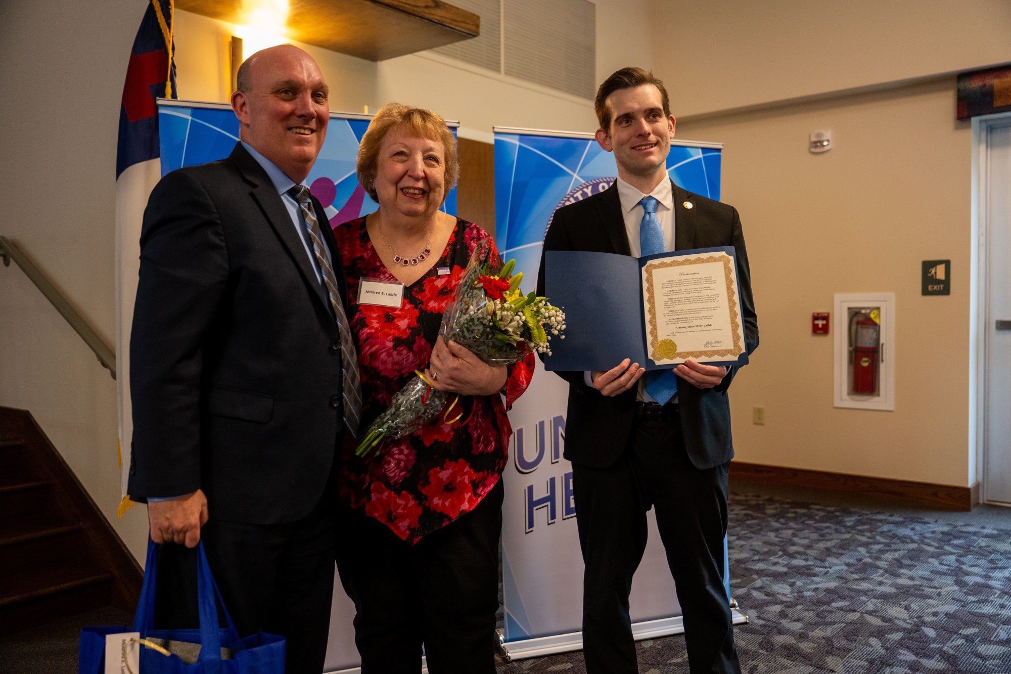 JR Reed of Lehigh County Aging & Adult Services and Lehigh County Executive Josh Siegel present an award to Milly Laible of Salisbury Township during the 26th annual Unsung Heroes tribute Wednesday, May 13, 2026, at Fellowship Community's Zentz Center in Whitehall Township. Laible is a volunteer leader with AARP Lehigh Valley. The annual tribute recognizes older adults who have enhanced their communities through active engagement, volunteerism and service to others. (Jonathan Broady/Special to The Morning Call)