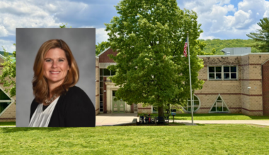 headshot of jennifer cierech, a woman with shoulder-length auburn hair wearing a black cardigan and white top, layered over a photo of calypso elementary school's brick entrance with a large tree and american flag in front