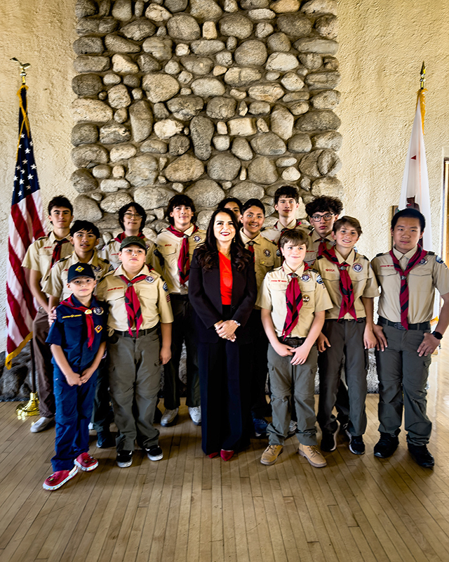| The South Pasadenan | South Pasadena News Group of scouts in tan uniforms with a female leader in a red blouse, posing indoors in front of a stone fireplace and Flags visible on either side.