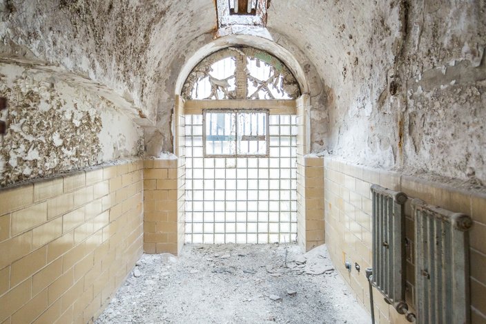 Prison room inside Eastern State Penitentiary with peeling white plaster and a curved door letting in sunlight