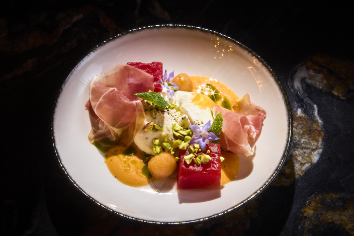 A burrata salad with melon and prosciutto on a white bowl