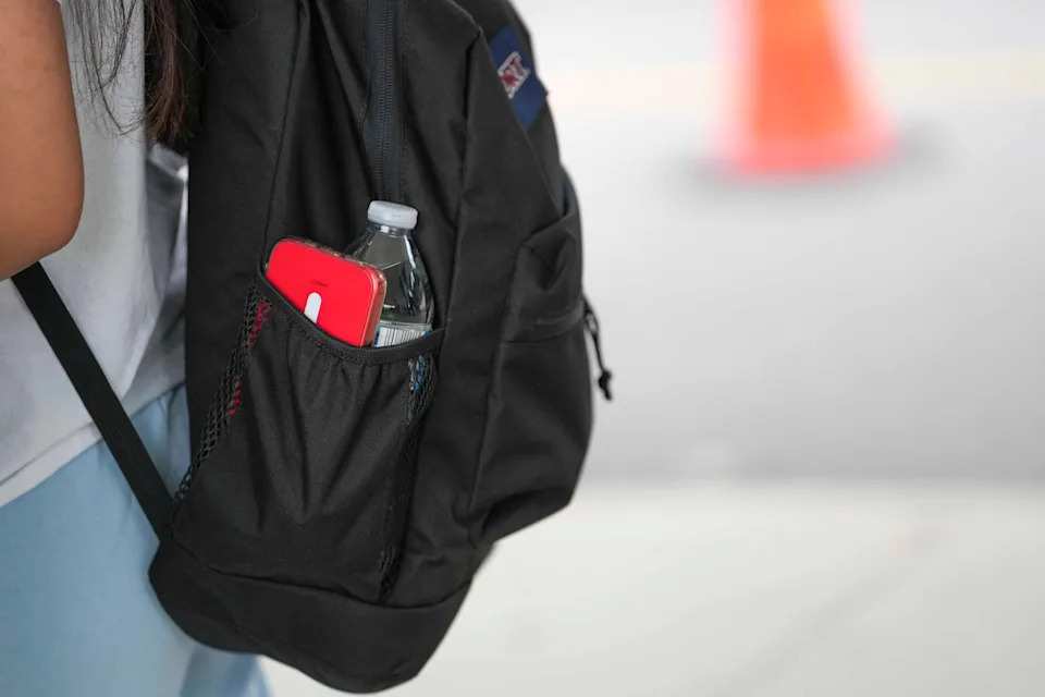 A student packs their cell phone in the side pocket of their backpack.