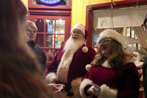 Dressed as Santa and Mrs., Claus, Gordon Crowell Jr. and Ellen Crowell greet people outside a restaurant in in Bethlehem, Pa., on Friday, Nov. 29, 2024. (AP Photo/Luis Andres Henao)