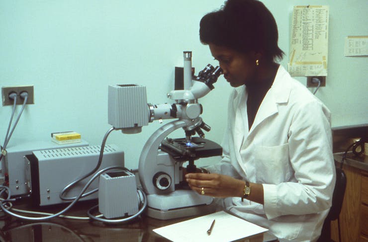 Woman in white lab coat looks through microscope