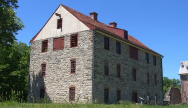 Old stone building with a red tile roof and red shutters under a clear blue sky.