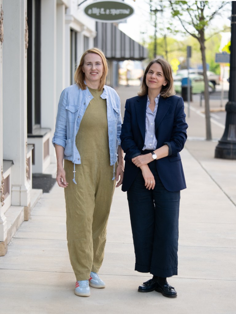 Two women in light jackets and pants standing on a street.