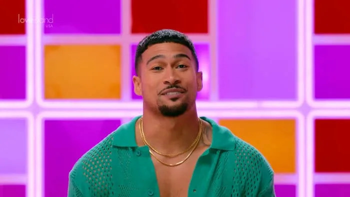 Person in a textured open shirt and layered necklaces, in front of a colorful geometric background