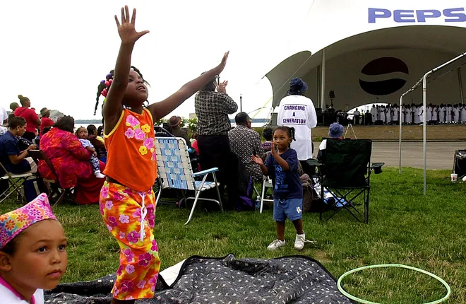 Erie resident Sheelae Bailey, 4, raises her arms during the music while Rachel Lyons, 4, claps along during the Port Erie Gospel Extravaganza at Liberty Park on Aug. 12, 2001. Chelsey Lyons, bottom left, listens while sitting on the lawn.