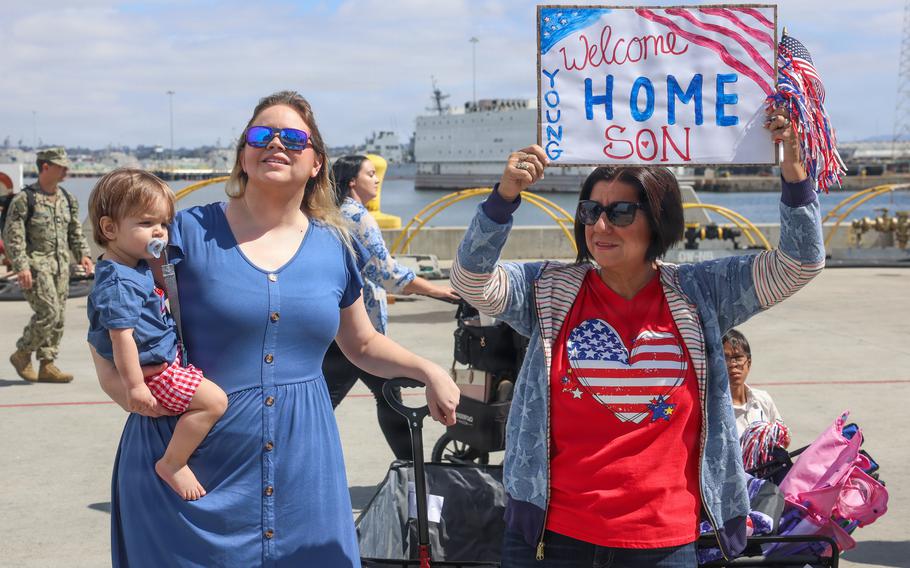 Two women await Lake Erie’s arrival. One holds a toddler, the other holds a sign that says welcome home son.