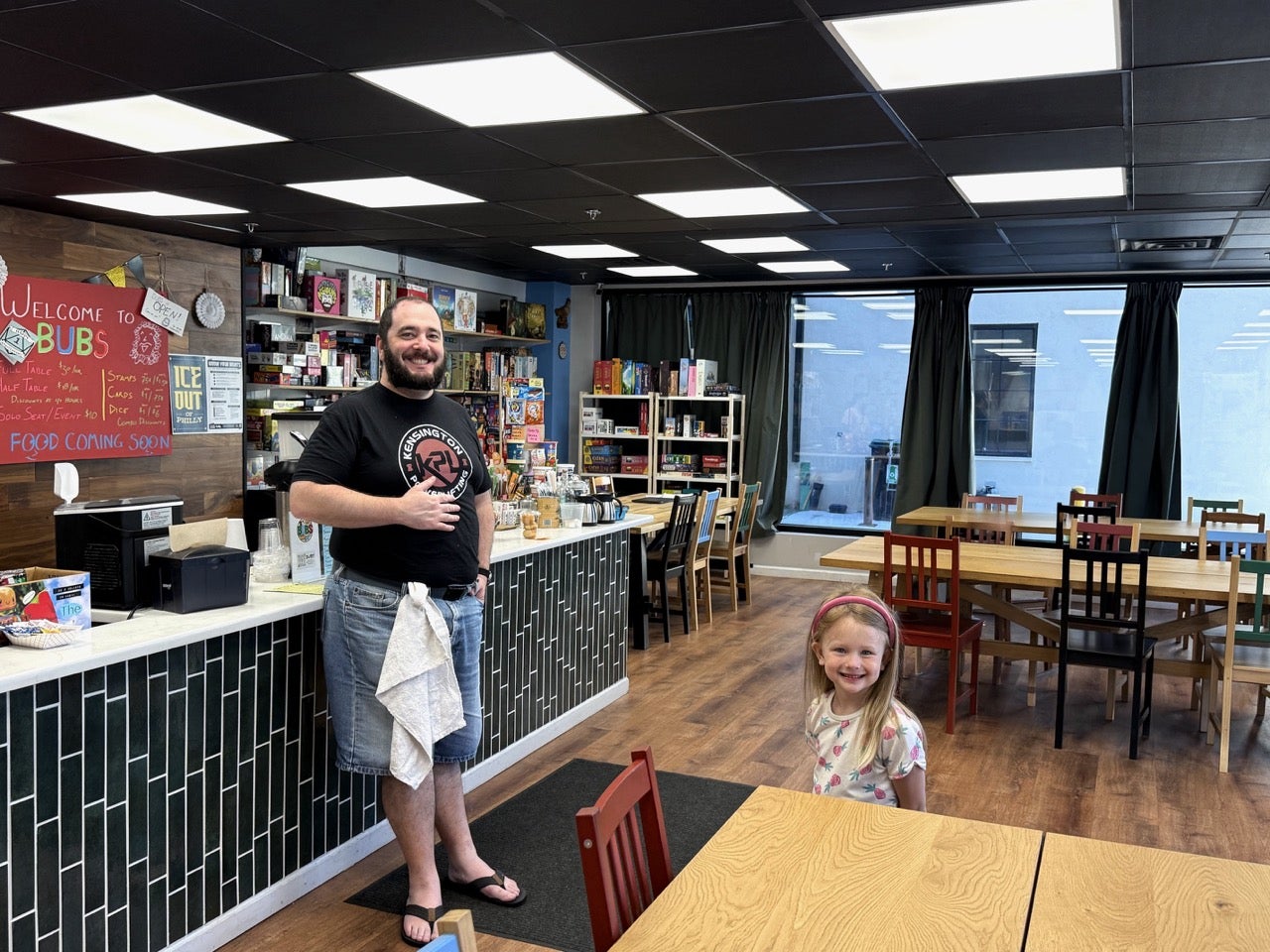 Simon from BUBS in Philadelphia standing next to the front counter and Kristen's daughter Trudy a few feet away from him smiling. 