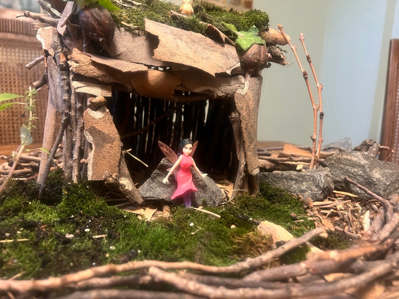 The Philly Fairy Festival at the Schuylkill Wildlife Center. A photo of Kristen and her kids' best try at making a fairy house of moss and twigs and leaves. There is a little plastic pink fairy out front.