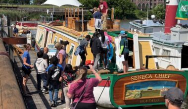 photo of a line of children and adults standing next to and walking onto a boat which reads seneca chief buffalo