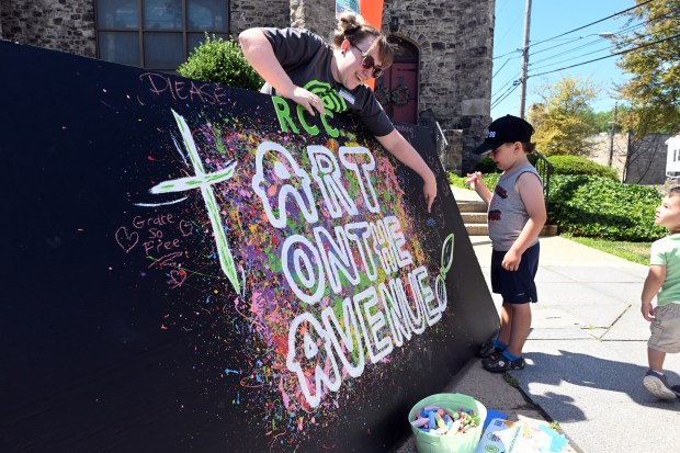 Savannah Cornelius, staff member at Reading City Church, points out a spot on which to doodle with chalk to Colt katkowski, 5, who was there with his mom Maria and brother, 1, all of Hamburg, during Art on the Avenue in West Reading on Saturday, June 20, 2026.    (BILL UHRICH/READING EAGLE)