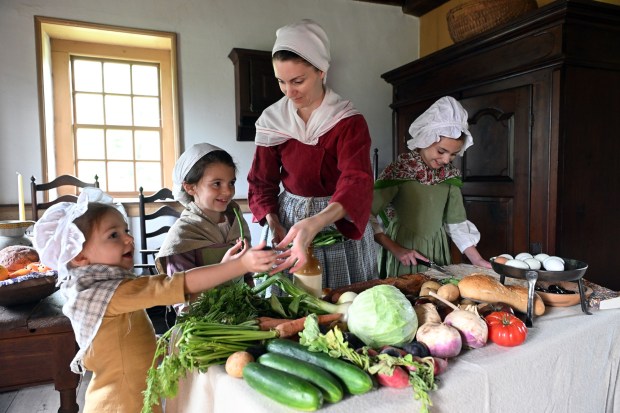 Brittany McMichael of Boyertown displays vegetables that would have been grown on a farm in the late 18th century with her children from left Ida, 4; Karolina, 8; and Eleanor, 11, during the Colonial 250th Anniversary Celebration at the Daniel Boone Homestead in Exeter Township on Saturday, June 27, 2026. (BILL UHRICH/READING EAGLE)