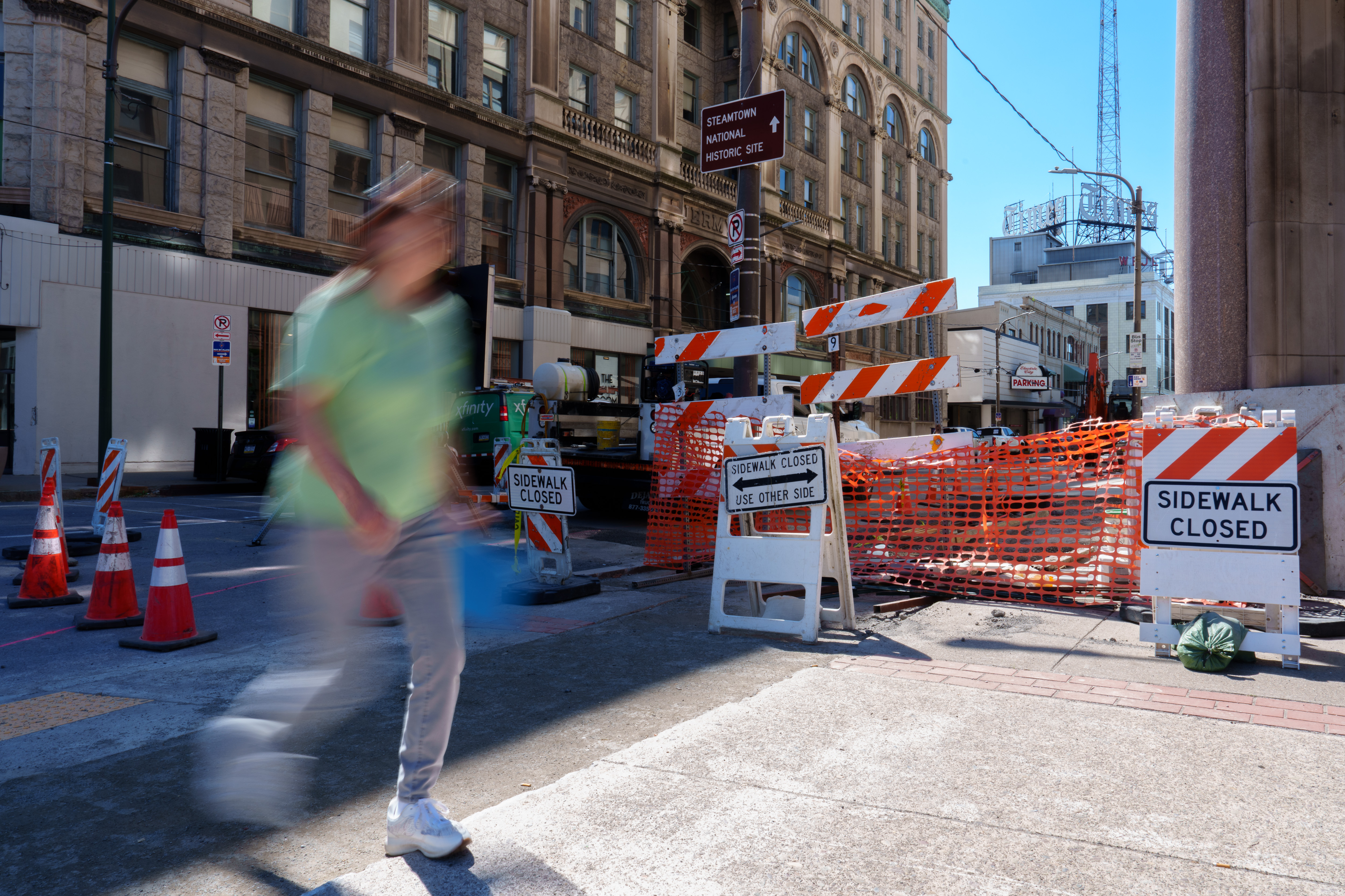A pedestrian walks past a closed sidewalk at the corner...