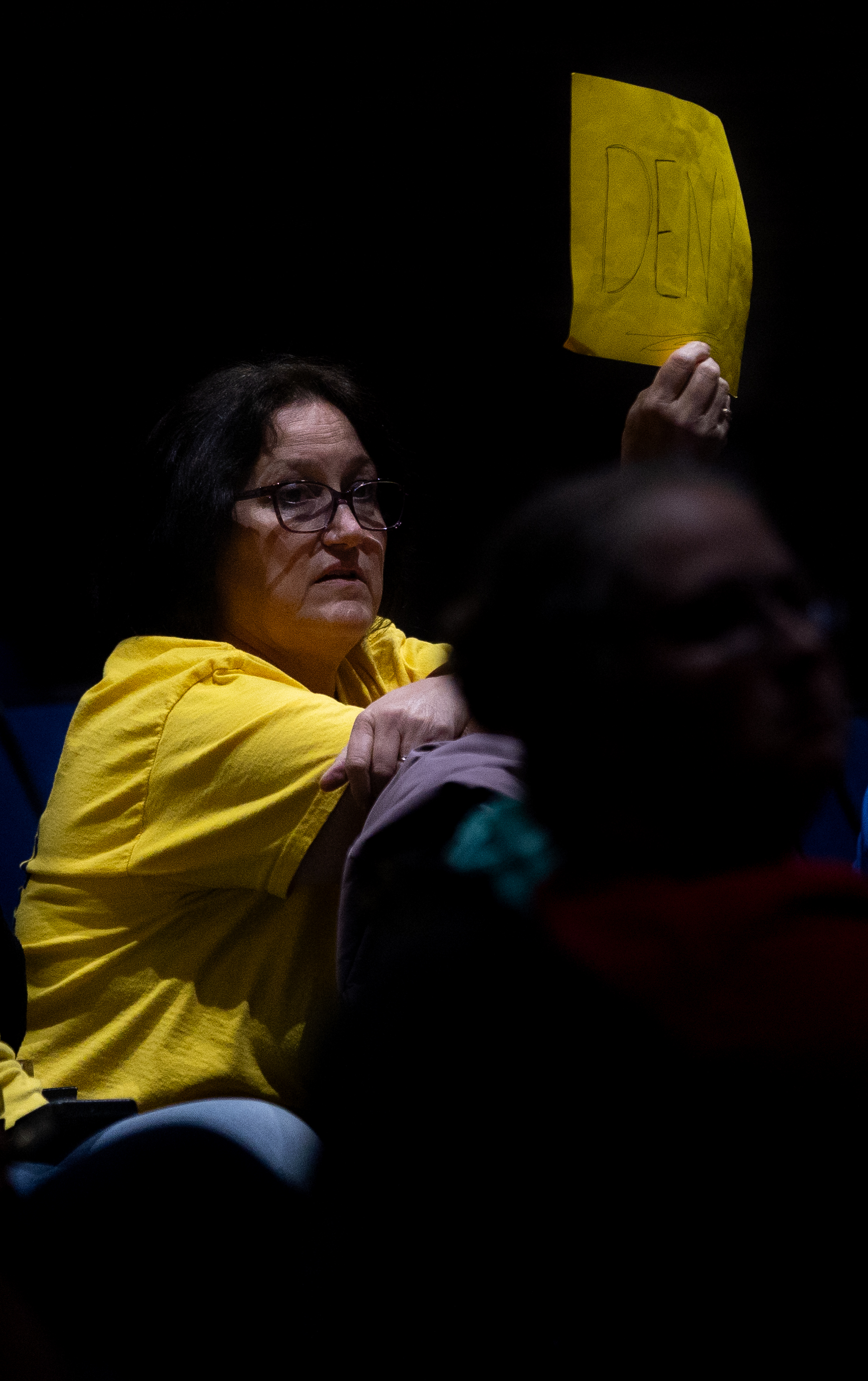 A woman holds a sign asking council to deny the...