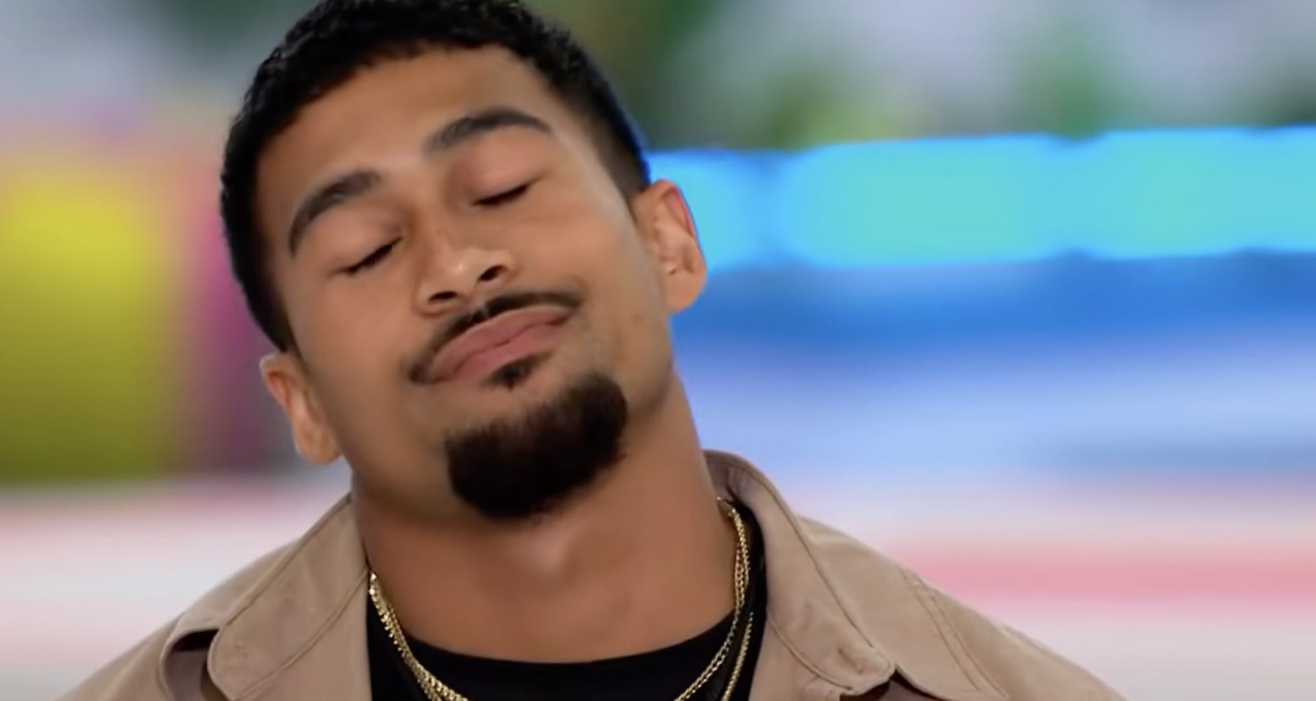Sean Reifel, a man with a goatee and gold chains, closes his eyes and tilts his head slightly.