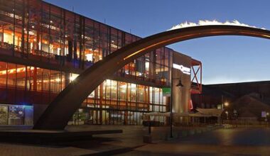 Night shot of a large steel arch with flames in front of a fully lit up multi-story glass buildingfront