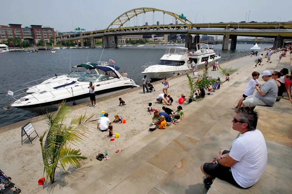 A group of people sitting along the bank of a river full of boats.