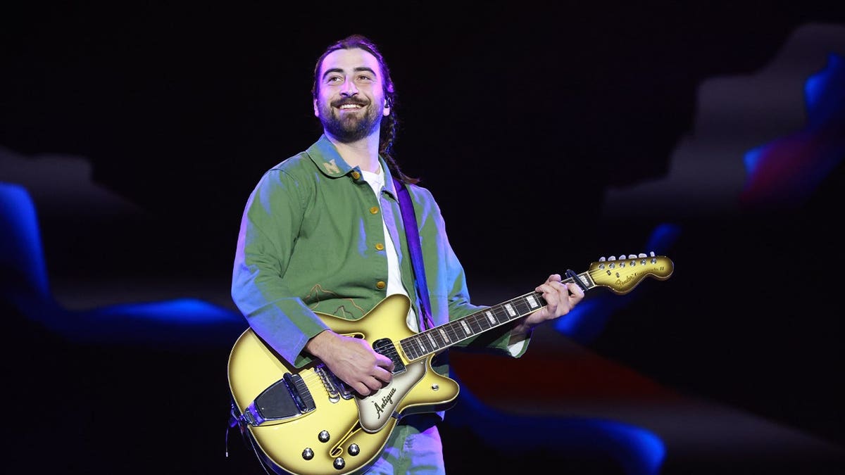 Noah Kahan holds guitar on stage