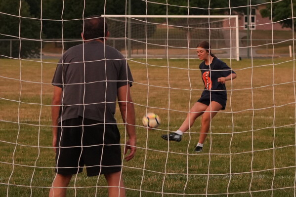 Cecelia Stefanelli, a rising freshman at Hershey High School, kicks a ball to score a goal against father, Justin Stefanelli, at a field where U.S. soccer national team star, Christian Pulisic, played when he was in school, in Hershey, Pa., on Tuesday, June 30, 2026. (AP Photo/Luis Andres Henao)