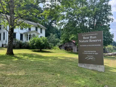 A sign for Bear Run Nature reserve in a yard of a white farmhouse.