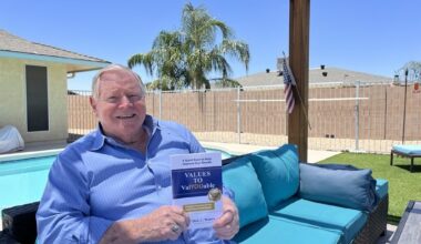 Sun City resident Dick Waters sits in his backyard holding one of his books.