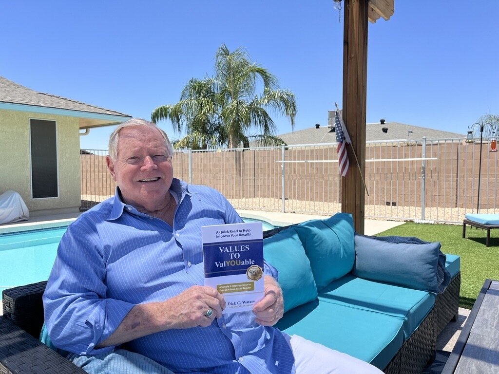 Sun City resident Dick Waters sits in his backyard holding one of his books.