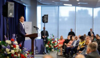 Governor Josh Shapiro in a suit speaking at podium during today's B+labs tour event with seated audience and floral arrangements.
