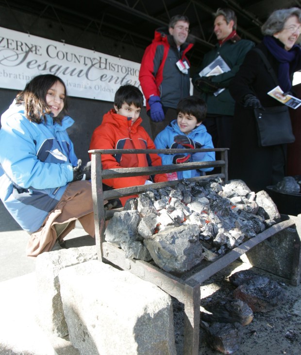 Descendants of Jesse Fell, from left, Samantha Teller Lottick, Kadan Edward Lottick and Antrim Ranjit Lottick warm themselves by an anthracite fire on a grate once used by their ancestor on the 200th anniversary of his discovery of a way to burn hard coal for home heating in 2008. (FILE PHOTO)
