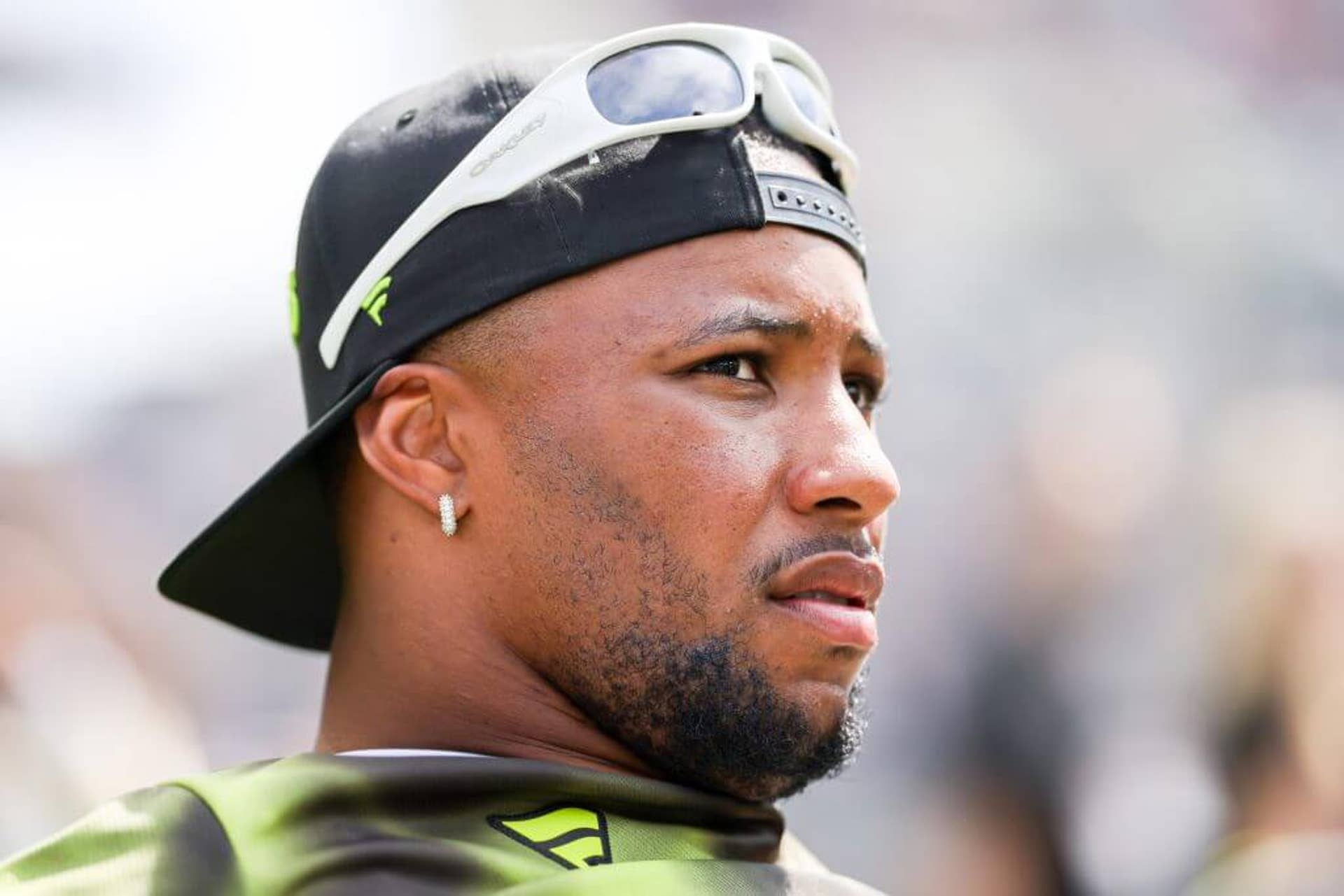 Saquon Barkley looks to his right while wearing a baseball cap backwards with sunglasses resting on his forehead.