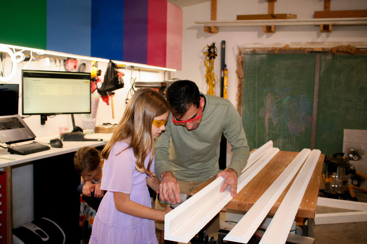 Joe Longstreet guides his daughter, Jane Longstreet, in using a nail gun in their home workshop.
