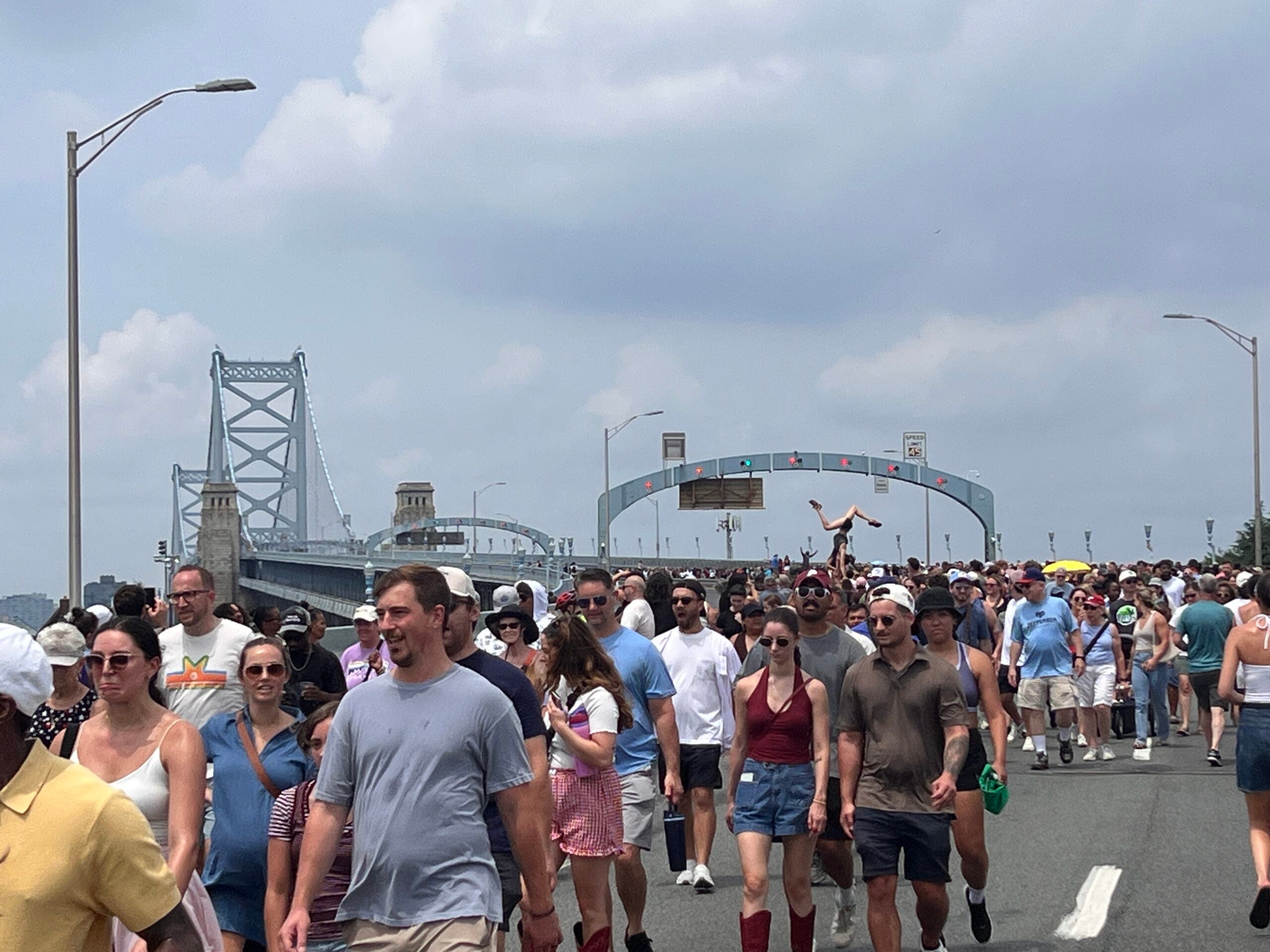 Thousands of people walked over the Ben Franklin Bridge on Saturday, July 11th to celebrate the 100th birthday of the Ben Franklin Bridge. The photo captures people arriving on the Camden side of the bridge. There is a person upside down on someone's shoulders off in the distance.