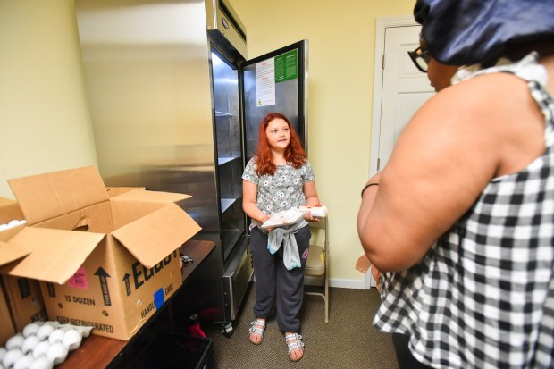 Volunteer Izabelle Wenrich, 10, hands eggs to a resident in the food pantry set up by the Friends of the Poor and Catherine McAuley Center at Hilltop Manor in Scranton's southside Monday, July 6, 2026. (SEAN MCKEAG / STAFF PHOTOGRAPHER)