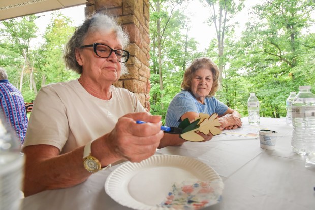 Diane Hiller, of Dickson City, paints a wooden ornament as Joan Buckas, of Throop, looks on during the "Fridays in the Park" kickoff event hosted by the Lackawanna County Area Agency on Aging at Aylesworth Park in Archbald Friday, July 10, 2026. (SEAN MCKEAG / STAFF PHOTOGRAPHER)