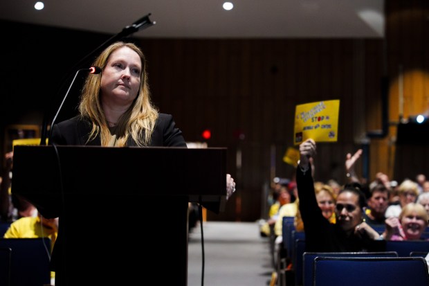 Attorney Megan S. Haines, representing the proposed Wildcat Ridge Data Center Campus, stands at a podium as an attendee in the background holds a sign that reads "STOP ARCHBALD DATA CENTERS" during a public hearing at Valley View High School in Archbald, Pa., on Monday, July 6, 2026. (ISAAC DIAZ/STAFF PHOTO)