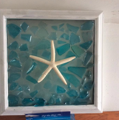 Framed glass art with a blue sea glass surrounding a starfish in the middle.